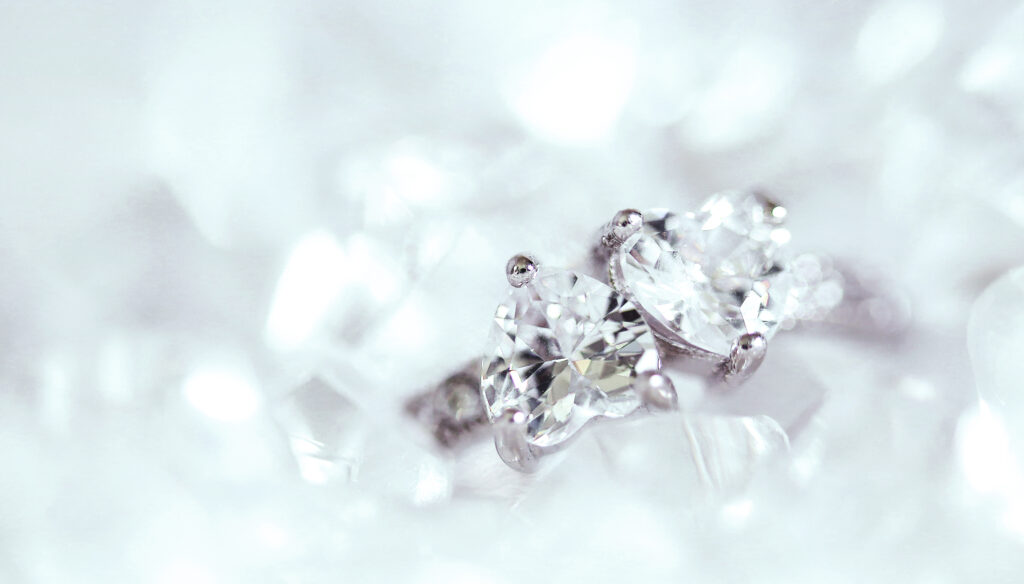 Close-up of two sparkling moissanite engagement rings with brilliant cuts, set in silver prongs, surrounded by a soft, white, blurred background for an elegant, luxurious look