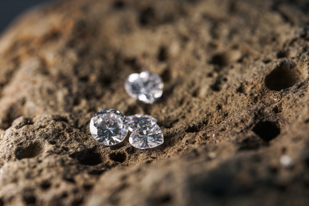 Round and heart-shaped moissanite gemstones displayed on a textured, porous rock surface, showcasing their brilliant clarity and eco-friendly appeal.