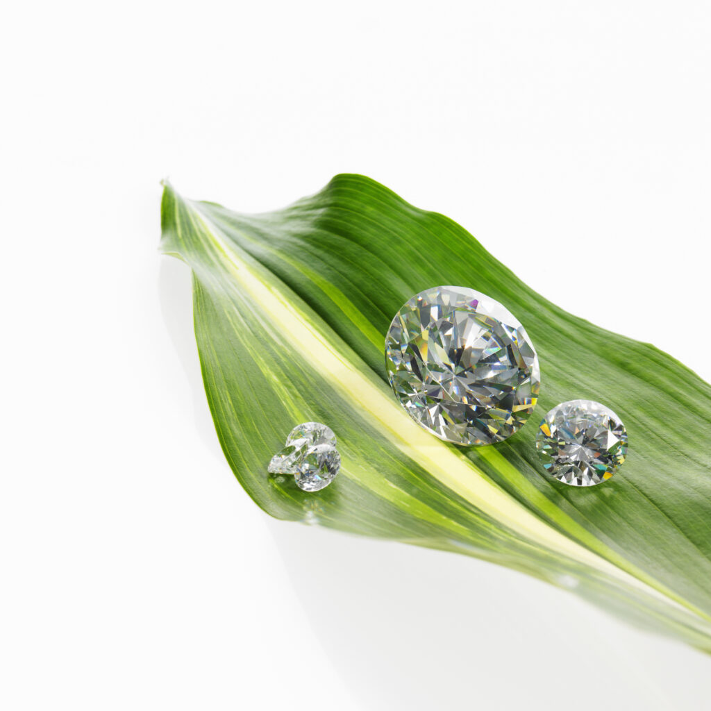 Three round brilliant-cut moissanite gemstones resting on a vibrant green leaf, symbolizing eco-friendly, sustainable luxury with exceptional clarity and sparkle.