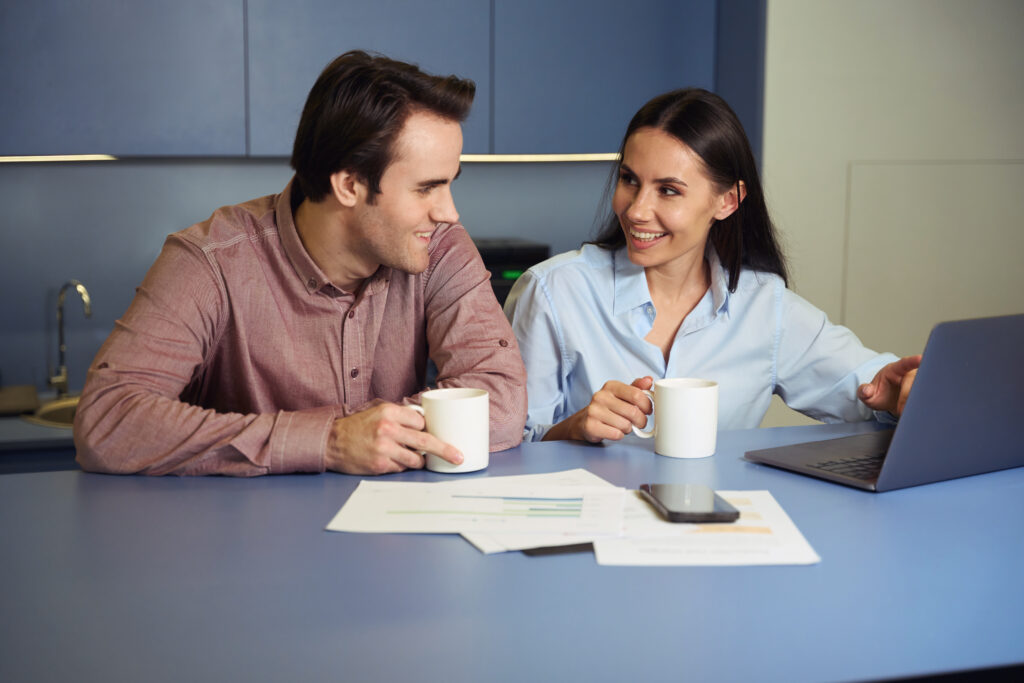 Smiling couple enjoying a cozy moment over coffee, discussing their future while admiring a stunning moissanite engagement ring, symbolizing love and commitment.