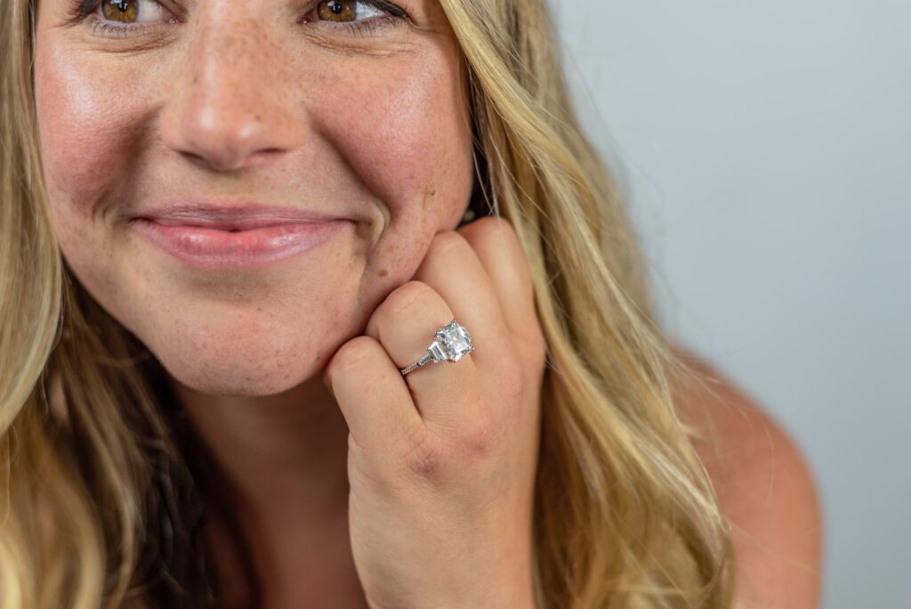 Smiling woman proudly showcasing her radiant-cut moissanite engagement ring with a sleek silver band, highlighting its brilliance and modern elegance.