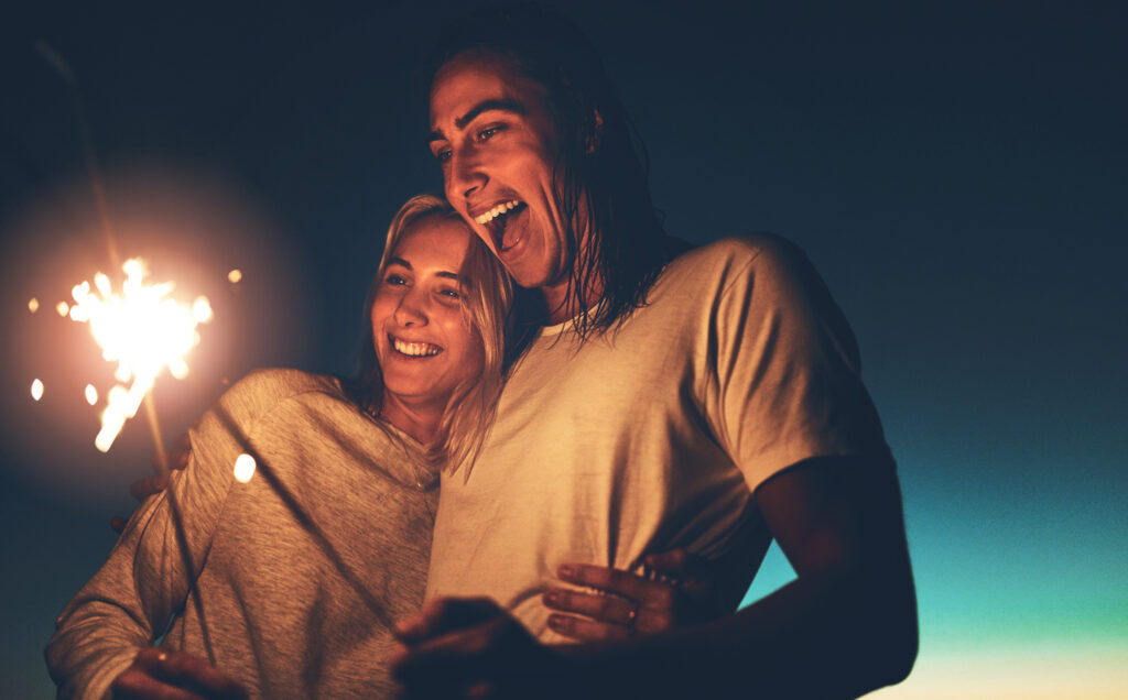 Smiling couple embracing under the night sky, holding sparklers, symbolizing love, joy, and celebration in a warm, intimate moment.