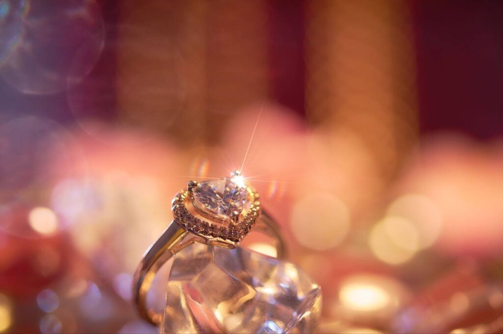 Heart-shaped moissanite engagement ring with a halo setting, elegantly displayed on a crystal with a warm, romantic bokeh background.